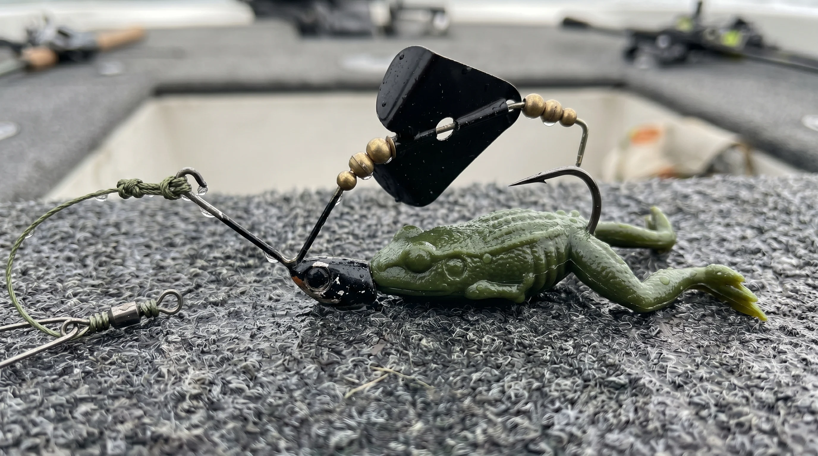 Close-up of a naked buzzbait rigged with a green soft plastic toad on boat deck